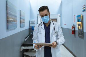 doctor wearing facemask and looking at clipboard in hands