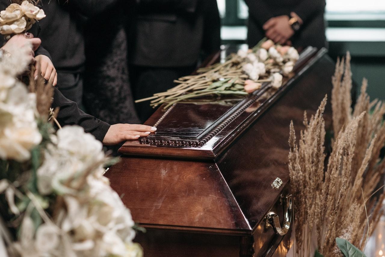person resting hand on coffin covered in flowers